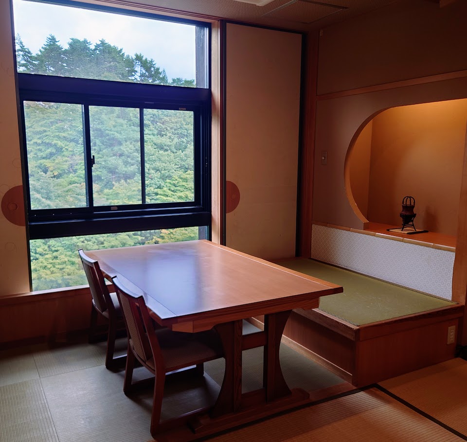 最上階和室の部屋の窓際には、大きなテーブルと座り心地のよい椅子がある。窓からは、美しい緑が見える。