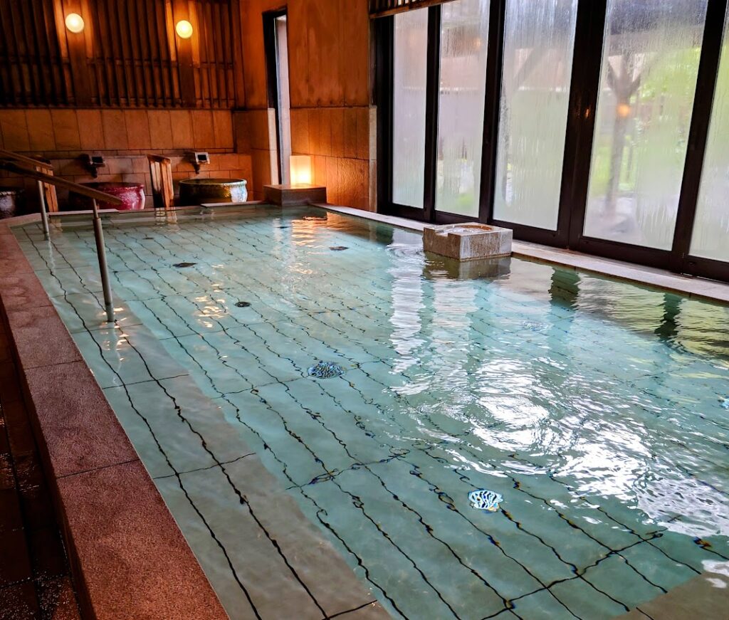 水上温泉「松乃井」の庭園風呂「蛍あかりの湯」の内湯から、窓越しに露天風呂が見える