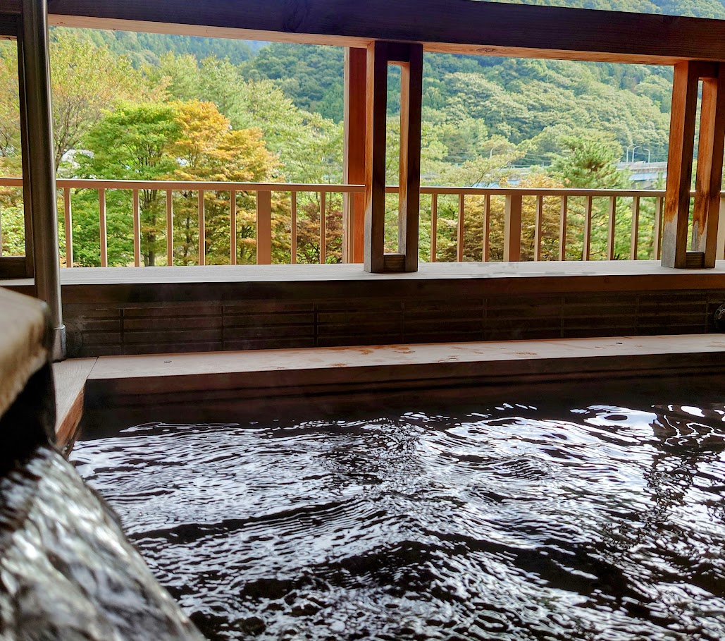 水上温泉「松乃井」の部屋の露天風呂には、勢いよく源泉が流れ込んでいる。窓枠からは、美しい景色が見えている。
