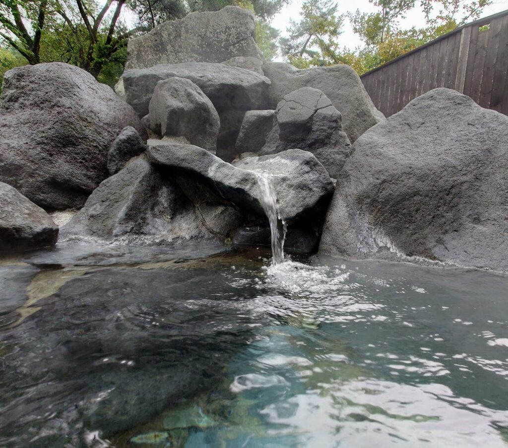 水上温泉「松乃井」の庭園風呂「蛍あかりの湯」の露天風呂は、大きな岩の間から温泉が噴き出している